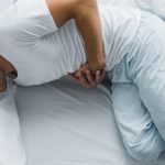 Ragazzo con maglia e pantaloni bianchi disteso su un letto con le mani sulla pancia e espressione dolorante