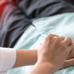 Mani di una dottoressa che visitano la pancia di un paziente disteso su un lettino