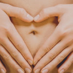 Dettaglio di mani femminili sulla pancia, che formano un cuore intorno all'ombelico