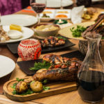 Tavolo imbandito per pranzo con piatti contenti carne e calici con vino rosso