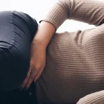 Donna distesa con la mano sulla pancia in posizione dolorante