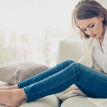 Ragazza seduta su un divano con le mani sulla pancia in posizione dolorante