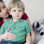 Mamma con un bambino in braccio che gli tocca la pancia, seduti su un divano