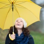 Donna che sorride sotto un ombrello giallo aperto