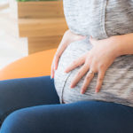 Dettaglio di donna in gravidanza con le mani sulla pancia, seduta su una poltrona