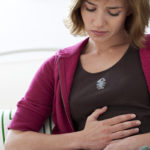 Donna con le mani sulla pancia con espressione facciale sofferente